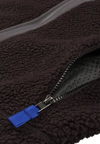 Tessuto in pile nero con una superficie testurizzata, dotato di una cerniera nera opaca e di un tirante in nylon blu su una tasca aperta.