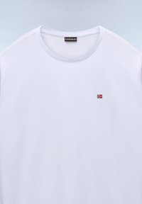 Tricou alb simplu, cu guler rotund, steag norvegian mic brodat pe partea stângă a pieptului și etichetă neagră în interiorul gulerului.