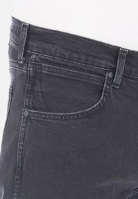 Černé džínové kalhoty s úzkým střihem, obsahující kapsu na mince, kontrastní prošívání a standardní design s pěti kapsami. Hladká textura.