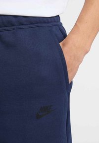 Granatowe bawełniane spodnie dresowe z elastycznym paskiem, bocznymi kieszeniami oraz czarnym logo Nike z przodu. Gładka tekstura, casualowy design.