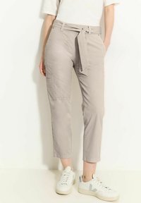 Pantalons beige courts avec une ceinture à nouer et des poches latérales, fabriqués en tissu doux. Assortis à des baskets blanches avec des accents gris.