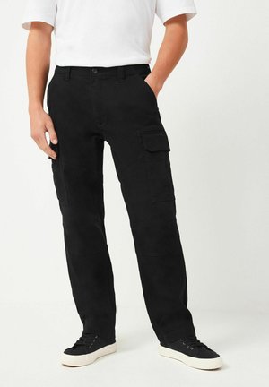 Pantaloni cargo negri, cu multiple buzunare, croi drept și material rezistent, asortați cu adidași negri și un tricou alb.