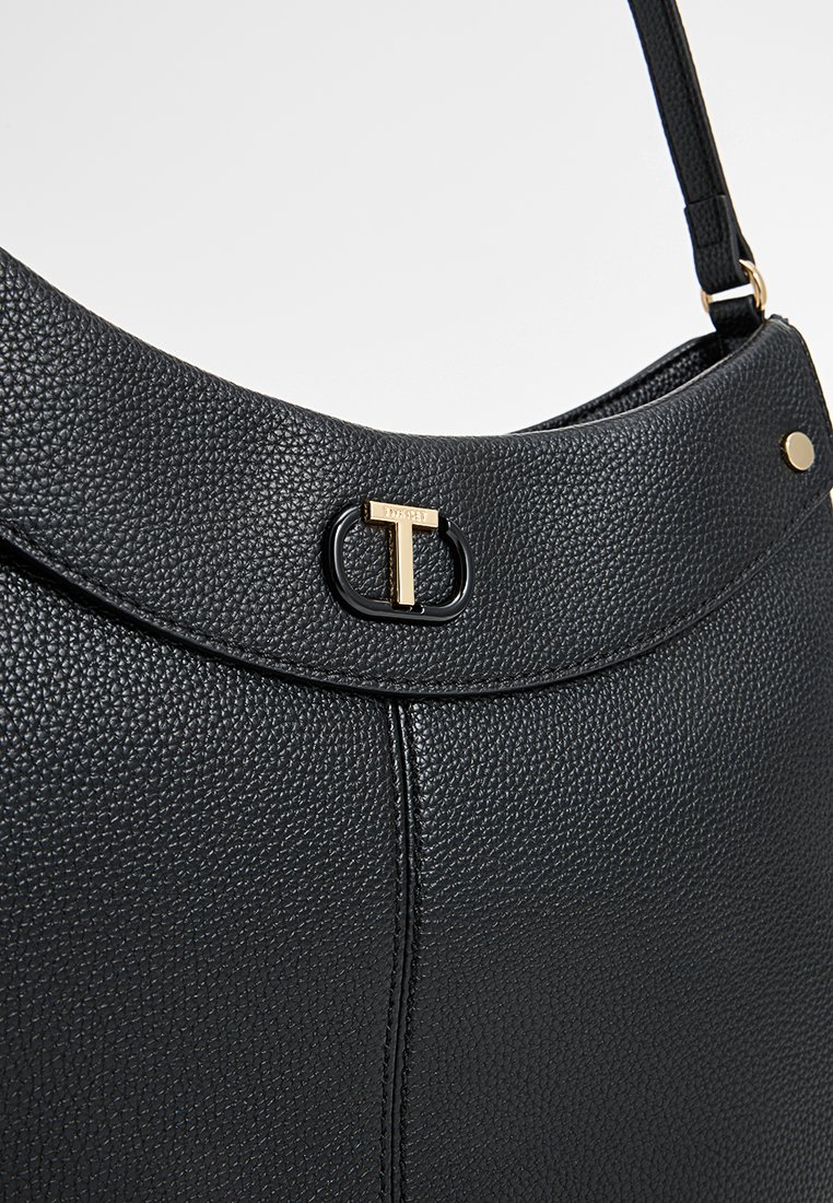 Bolso de mano de cuero negro con un acabado texturizado, que presenta un logo en tono dorado con forma de "T" y un diseño elegante. Incluye una correa para el hombro y un hardware minimalista.