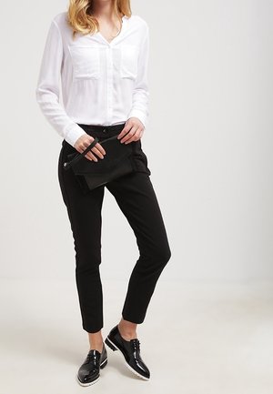 White long-sleeve blouse with button-up front, two chest pockets, black fitted pants, black clutch bag, and shiny black shoes.