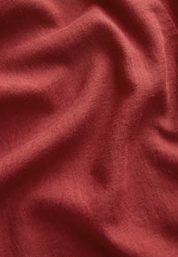 Puha, gyűrött mélyvörös szövet látható szövött textúrával, finom redőkkel, amelyek árnyékokat és fényeket hoznak létre.