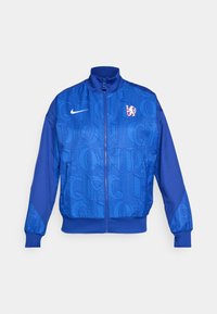 Plava jakna na zip s teksturiranim uzorkom na kojem se nalaze natpisi "LONDON" i "CFC," Nike logo, visoki ovratnik i elastične manžete.