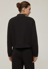 Felpa nera a maniche lunghe con collo alto, polsini a coste e una texture liscia. Presenta un design pulito e minimalista senza loghi visibili.