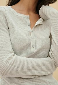 Lichtgrijze ribgebreide trui met een henley halslijn, vier decoratieve knopen en lange mouwen met textuurdetails.