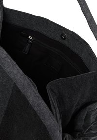 Czarna torba materiałowa w odcieniu ciemnoszarym, otwarta, aby pokazać wnętrze z zamykaną na zamek kieszenią oraz zapięciem na magnes na górnej krawędzi.