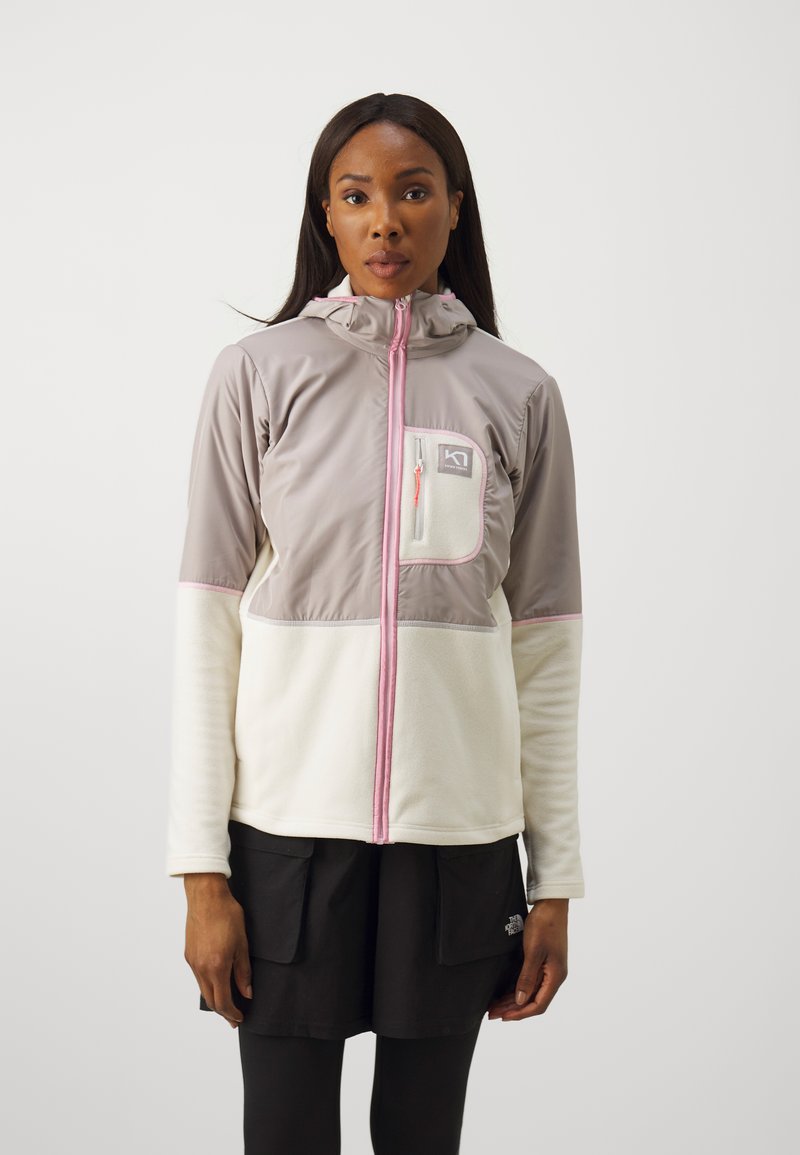 Ελαφρύ μπουφάν με γκρι απαλό πανί στην πάνω πλευρά, κρεμ φλις στο κάτω μέρος, μια μπροστινή τσέπη και ροζ λεπτομέρειες κατά μήκος του φερμουάρ και του ρέλι.
