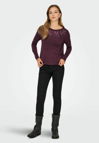 Pull en maille bourgogne à manches longues, avec des détails embellis sur le devant. Associé à un jean noir ajusté et des bottes noires montantes.