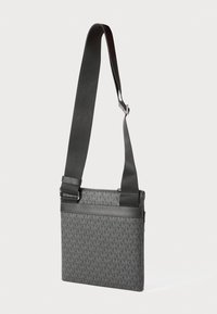 Sac en bandoulière noir avec un motif texturé mettant en avant la lettre 'M', bandoulière réglable et fermeture éclair. Accents en cuir lisse.