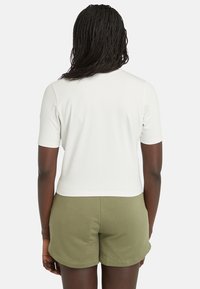 Top blanco de manga corta con corte recto y escote redondo, combinado con pantalones cortos de color verde oliva, con una textura suave.