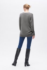 Grau gestrickter Pulli, leicht oversized, mit langen Ärmeln und gerippten Bündchen. Getragen mit blauen Jeans und schwarzen kniehohen Stiefeln. Schlichter Hintergrund.