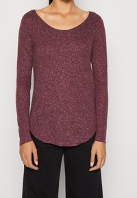 Camicia bordeaux a maniche lunghe con scollatura a girocollo, realizzata in tessuto testurizzato, con orlo curvo e vestibilità slim. Abbinata a pantaloni neri.