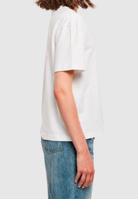 Bílé bavlněné tričko s krátkými rukávy, volný střih a růžovým grafickým designem na přední straně. V kombinaci se světle modrými džínami.