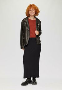 Schwarze Lederbikerjacke, rot gestreiftes Langarmoberteil, schwarze Maxiröhre und schwarze Stiefeletten. Glatte Texturen und geschichtetes Design.