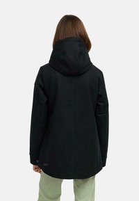 Veste noire à capuche en tissu texturé, avec un dos légèrement plus long, des poches sur les côtés et un logo discret sur l'ourlet.