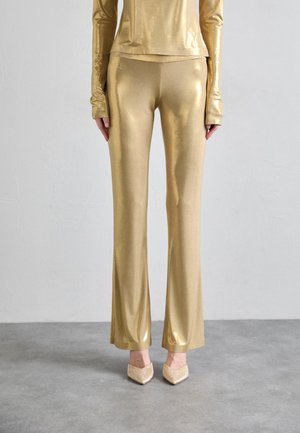Gold metallic long-sleeve top and flared pants, featuring a smooth, shiny texture. Finished with pointed, embellished shoes.
