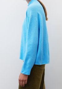 Pull tricoté bleu clair avec un col montant, des poignets et un ourlet côtelés, présentant une coupe décontractée et une texture douce, assorti à un pantalon en velours côtelé olive.