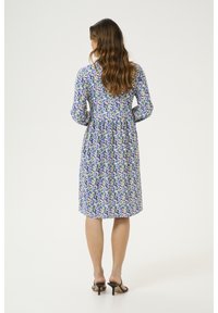 Kukallinen mekko violetin, vihreän ja valkoisen värin yhdistelmässä; puolipitkä, kerätty vyötärö ja pitkät hihat. Yhdistetty mustien korkokenkien kanssa.