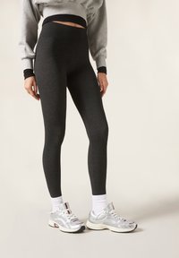 Schwarze, hoch taillierte Leggings aus dehnbarem Stoff, kombiniert mit silbernen Sportschuhen und weißen Kniestrümpfen. Glatte Textur, enganliegendes Design.