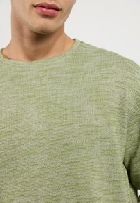 Pull léger vert texturé avec un col rond, présentant un motif chiné subtil et un tissu doux et respirant.