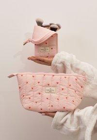 Vadderade rosa sminkväskor med röda hjärtan mönster. Den större väskan har en dragkedjestängning, medan den mindre har en halv dragkedjedesign.