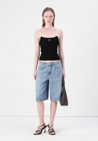 Svart strikket tanktop med hvite stropper, med utklipp formet som et hjerte. Lyseblå denimshorts til kneet og svarte høyhælte sandaler med stropper.