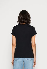 Juodas trumpas rankovės marškinėliai su apvaliu iškirpimu. Minkšta medžiaga ir tiesus siluetas. Atgalinis vaizdas rodo trumpas rankoves ir paprastą dizainą.