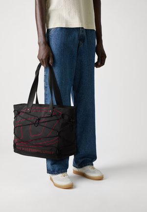 Sac fourre-tout noir avec des accents rouges et un design en bungee, fabriqué en matériau durable. Dispose de poignées plates robustes et d'un intérieur spacieux.