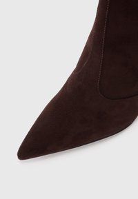 Brown suede ankle boot with a pointed toe and a sleek design. Features subtle stitching along the side panel for added detail.