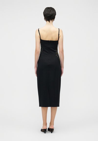 Fekete testhezálló ruha vékony pántokkal, középikarbeli hosszúsággal, hátul függőlegesen elhelyezett díszítő kristályokkal. Sima anyag textúra.