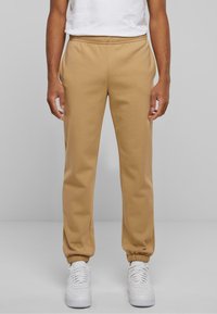 Beige Jogginghosen aus weichem Material mit einem elastischen Bund und Bündchen. Mit seitlichen Taschen gestaltet, kombiniert mit weißen Sneakers.
