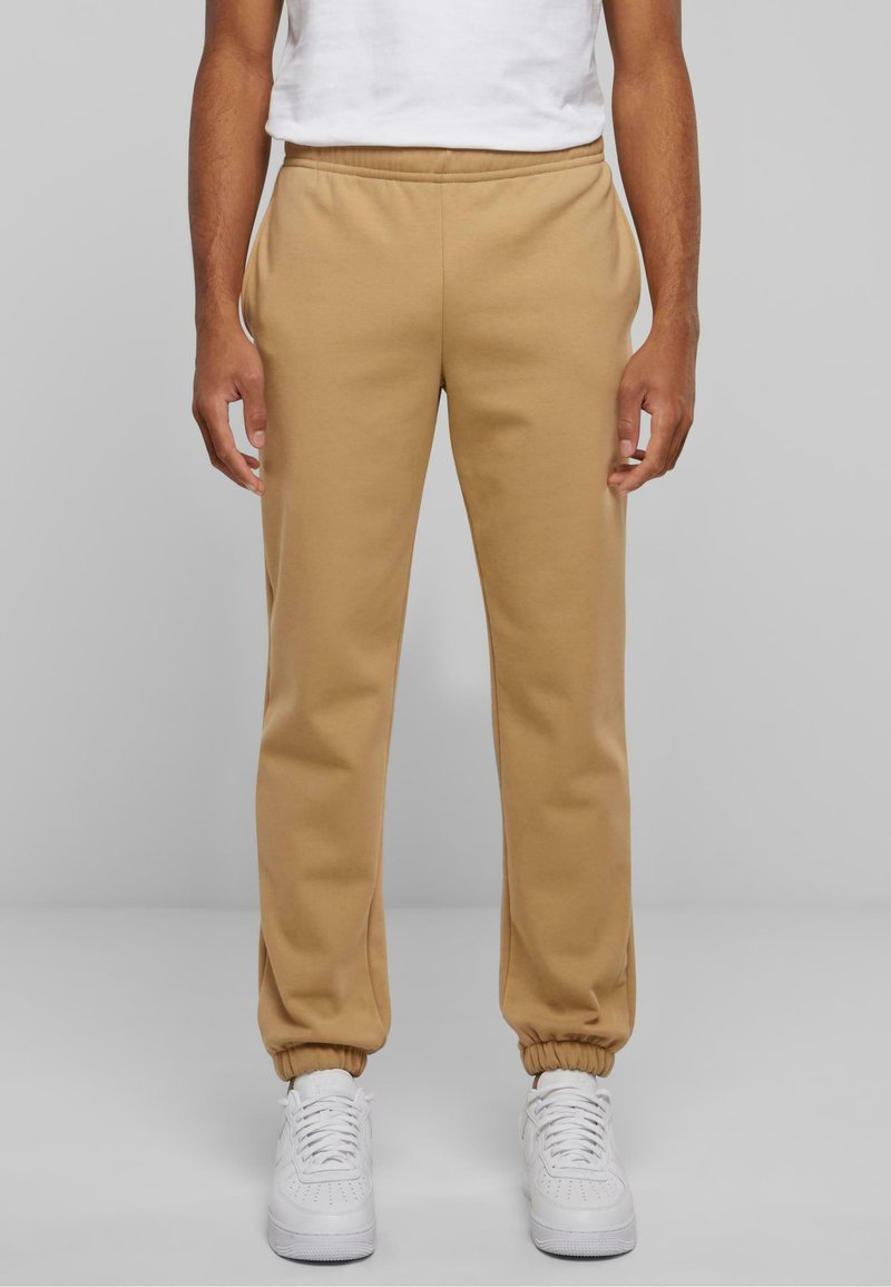 Beige Jogginghosen aus weichem Material mit einem elastischen Bund und Bündchen. Mit seitlichen Taschen gestaltet, kombiniert mit weißen Sneakers.