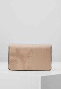 Béžová peněženka s texturovaným hadím vzorem umístěná na bílém podstavci na jednodeskovém světle šedém pozadí.