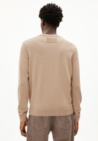 Beiger gestrickter Pullover mit langen Ärmeln, Rundhalsausschnitt und gerippten Bündchen. Verfügt über einen strukturierten Einsatz am Nacken hinten. Getragen mit Cordhosen.