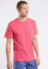 T-shirt à col rond à manches courtes en corail vif, en coton, avec un petit logo bleu sur la poitrine gauche et une coupe décontractée.