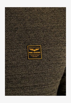 Donkergroen gestructureerde trui met een geel en zwart label met de tekst "PME LEGEND" en "GETEST OP GROTE HOOGTE."