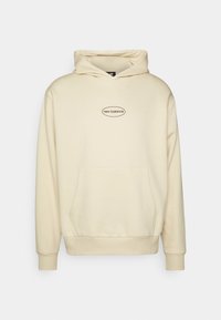 Felpa color crema realizzata in tessuto morbido. Presenta una tasca frontale, polsini a costine e il logo 'New Balance' in design ovale sul petto.