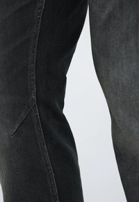 Detailný záber na čierne denimové nohavice s konečným bočným šitím a textúrovanou tkaninou.