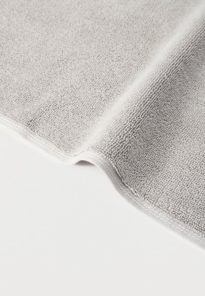 Ανοιχτό γκρι υφασμάτινο πανί μικροϊνών με υφή, διπλωμένο πάνω σε λευκή επιφάνεια, που δείχνει απαλό, πλεκτό ύφασμα με ραμμένες άκρες.