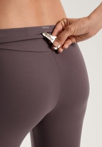 Legginsy o wysokim stanie, elastyczne, w ciemnym mauve z dyskretną kieszonką na suwak z tyłu pasa, do przechowywania małych przedmiotów.