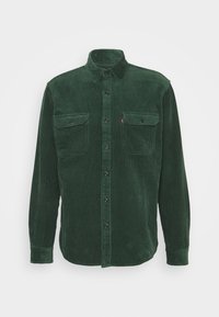 Tummanvihreä samettipaita, jossa on napit ja pitkät hihat, sekä kaksi nappikiinnitys taskua rinnalla, valkoista taustaa vasten.