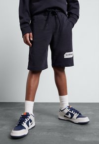 Marineblauwe katoenen shorts met een elastische tailleband, zijzakken en een wit label op de zoom. Gepaard met witte sokken en multikleurige sneakers.