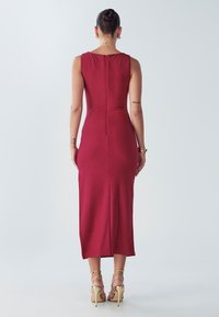 Pieguļošas bordo krāsas kleita ar rāvējslēdzēju mugurpusē, ceļgalu garuma, gludas tekstūras, bez piedurknēm, kombinēta ar zelta krāsas siksniņu papēžiem.