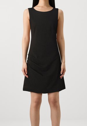 Robe noire sans manches longueur genou avec encolure ronde et détails de boutons sur les côtés portée par une personne debout devant un fond uni.