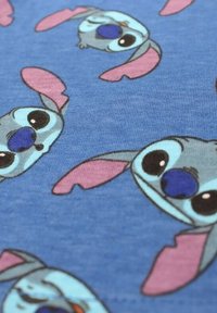 Tissu bleu orné de multiples visages de dessin animé de Stitch de Lilo & Stitch, montrant de grands yeux et des oreilles roses dans diverses orientations.