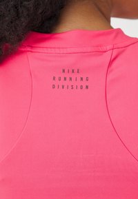Top deportivo de color fucsia con un cuello redondeado y costuras planas, con "NIKE RUNNING DIVISION" impreso en negro en la parte posterior.