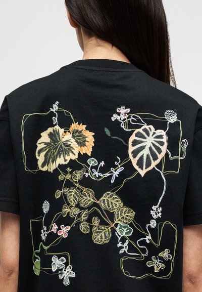 Μαύρο μπλουζάκι με περίτεχνα κεντημένα σχέδια από λουλούδια και φύλλα σε διάφορα χρώματα, με ορατά περιγράμματα και λεπτομέρειες φυτών στην πλάτη.